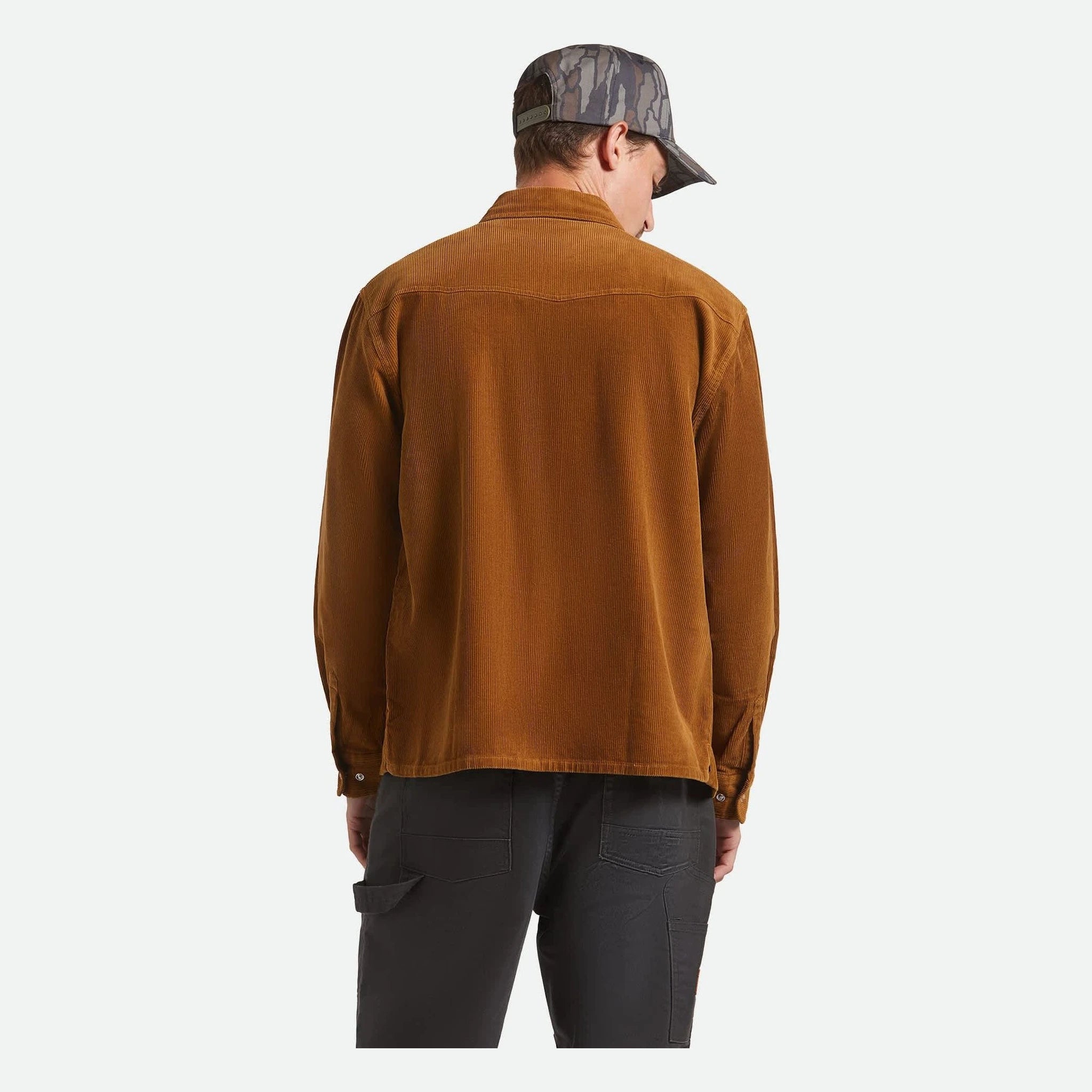 Person wearing New West Relaxed Overshirt Washed Copper Cord Jacket, Man wearing copper corduroy overshirt against neutral