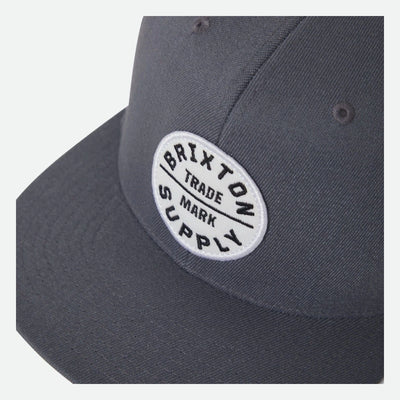 Close-up of Oath III Snapback Khaki/primal Green Hat showing White oval embroidered patch with black text reading "Brixton