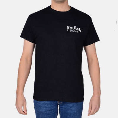 Person wearing Paisley Black Tee, Man wearing black tee with white chest print, standing in neutral studio setting -
