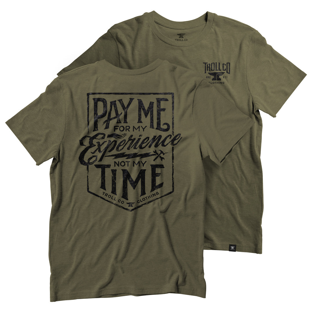 Close-up of Pay Me Military Tee showing Military green with dark navy distressed print in shield-shaped badge layout, script