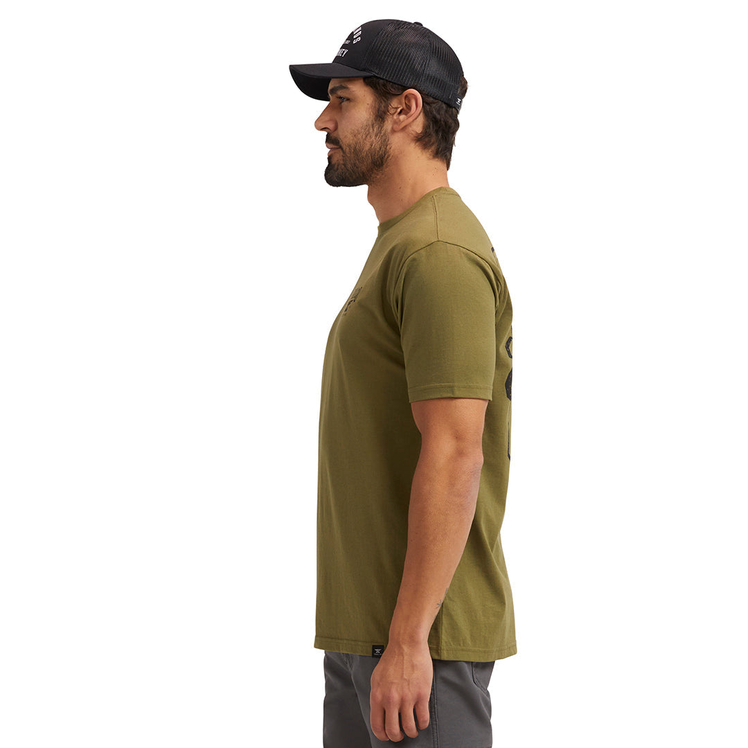 Person wearing Pay Me Military Tee, Man wearing military green tee against neutral white backdrop - Slowride Supply
