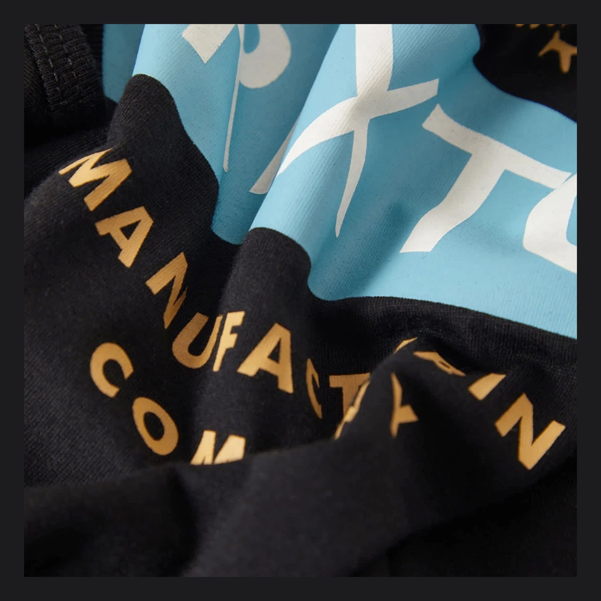 Close-up of Pinnacle Tank Top Apparel Black Apparel showing Gold embroidered lettering and cream ribbed knit collar tag