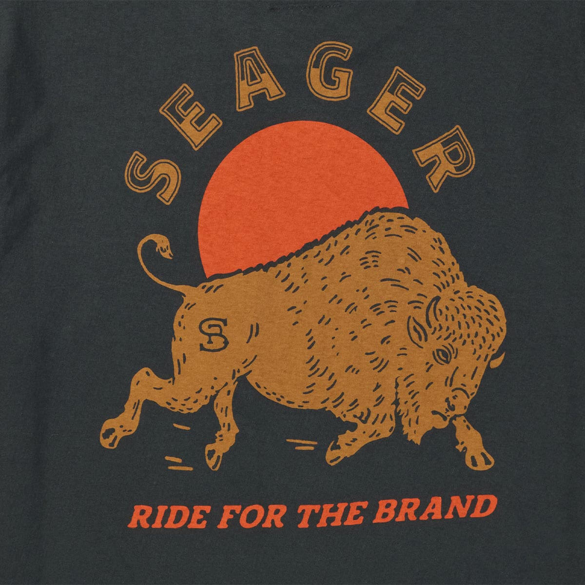 Close-up of Ride for the Brand Vintage Black Tee showing Tan outline letters spelling "SHEAGER" arcing above a gold bull