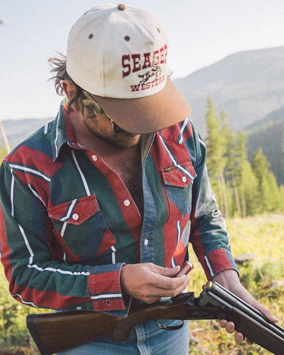 Person wearing Rodeo Snapback Cream/brown Hat, Mountain landscape with evergreen trees and rolling hills in background -