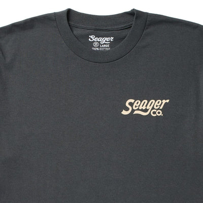 Close-up of Romero White Tee showing Charcoal tee with cream script logo across chest, ribbed crewneck collar, 100% cotton