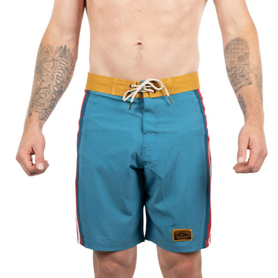 Person wearing Skeg 19" Boardshort Apparel Indigo Apparel, Shirtless man wearing board shorts against white studio
