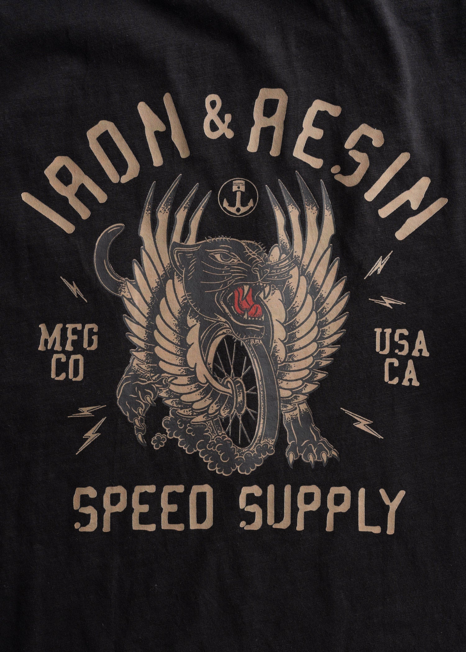 Close-up of Speed Supply Black Tee showing Tan and red winged beast graphic with anchor, lightning bolts, and text detail -