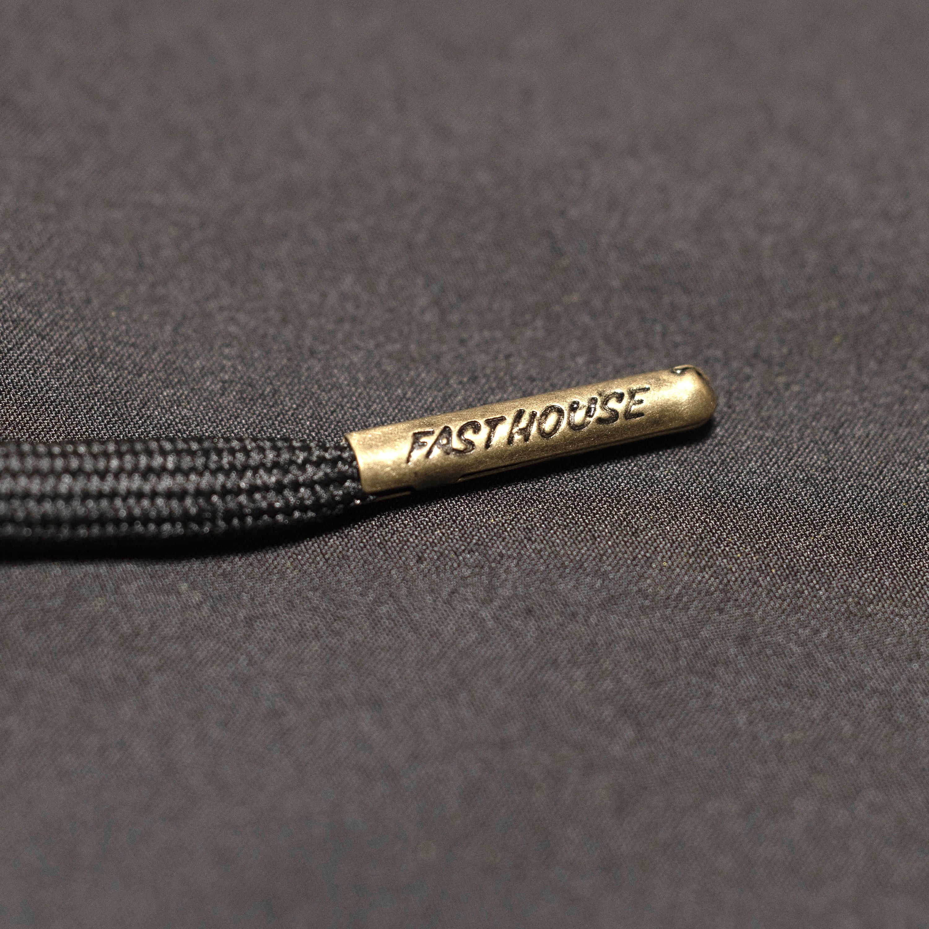 Close-up of Stealth 21" Boardshort Boardshorts Black Boardshorts showing Brass aglet with "FASTHOUSE" text stamped on black