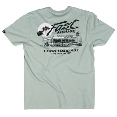Close-up of Sunset Black Tee showing Sage green with black line-art graphic depicting vintage auto dealership storefront,