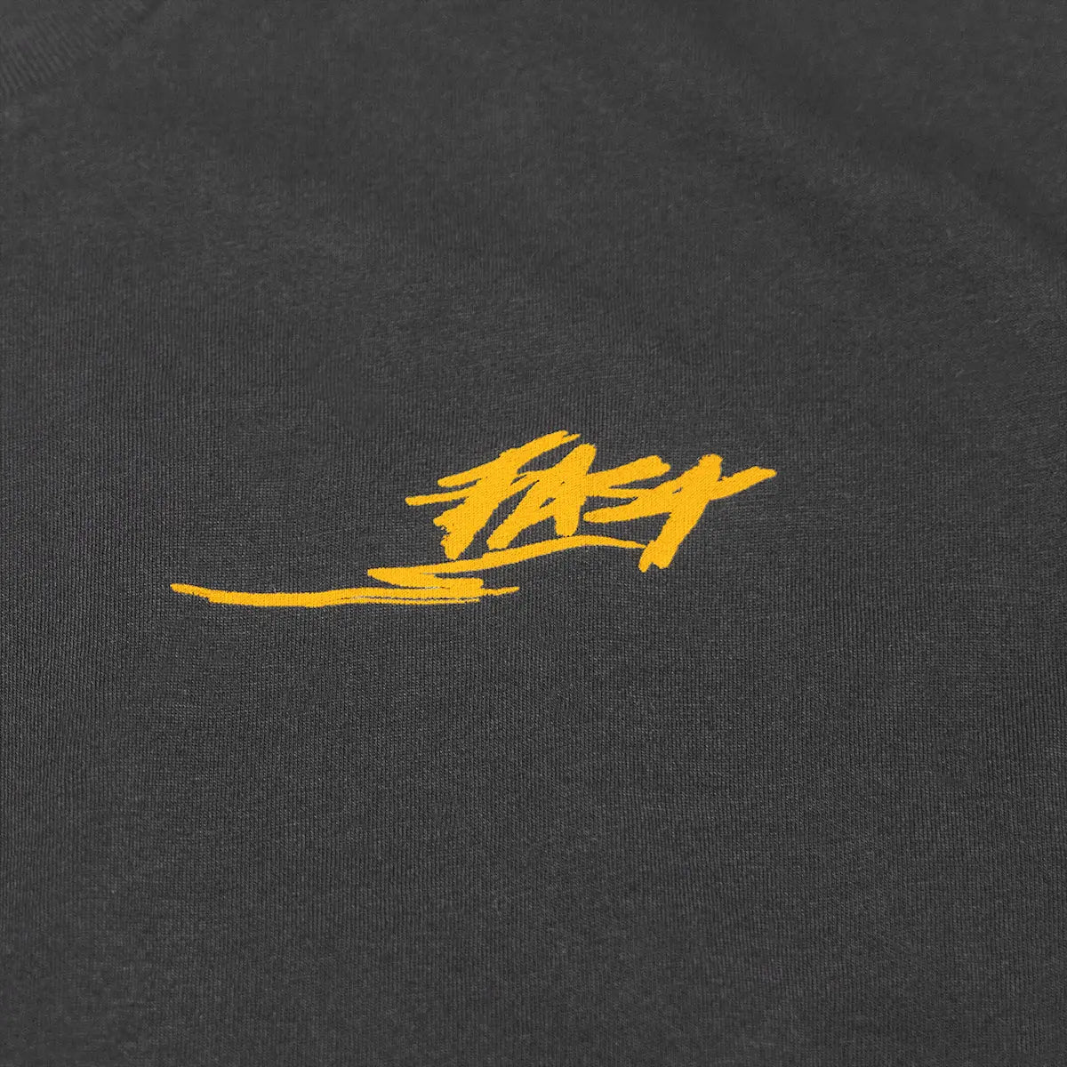 Close-up of Tomahawk Natural Tee showing Gold embroidered script logo on charcoal cotton jersey with directional underline