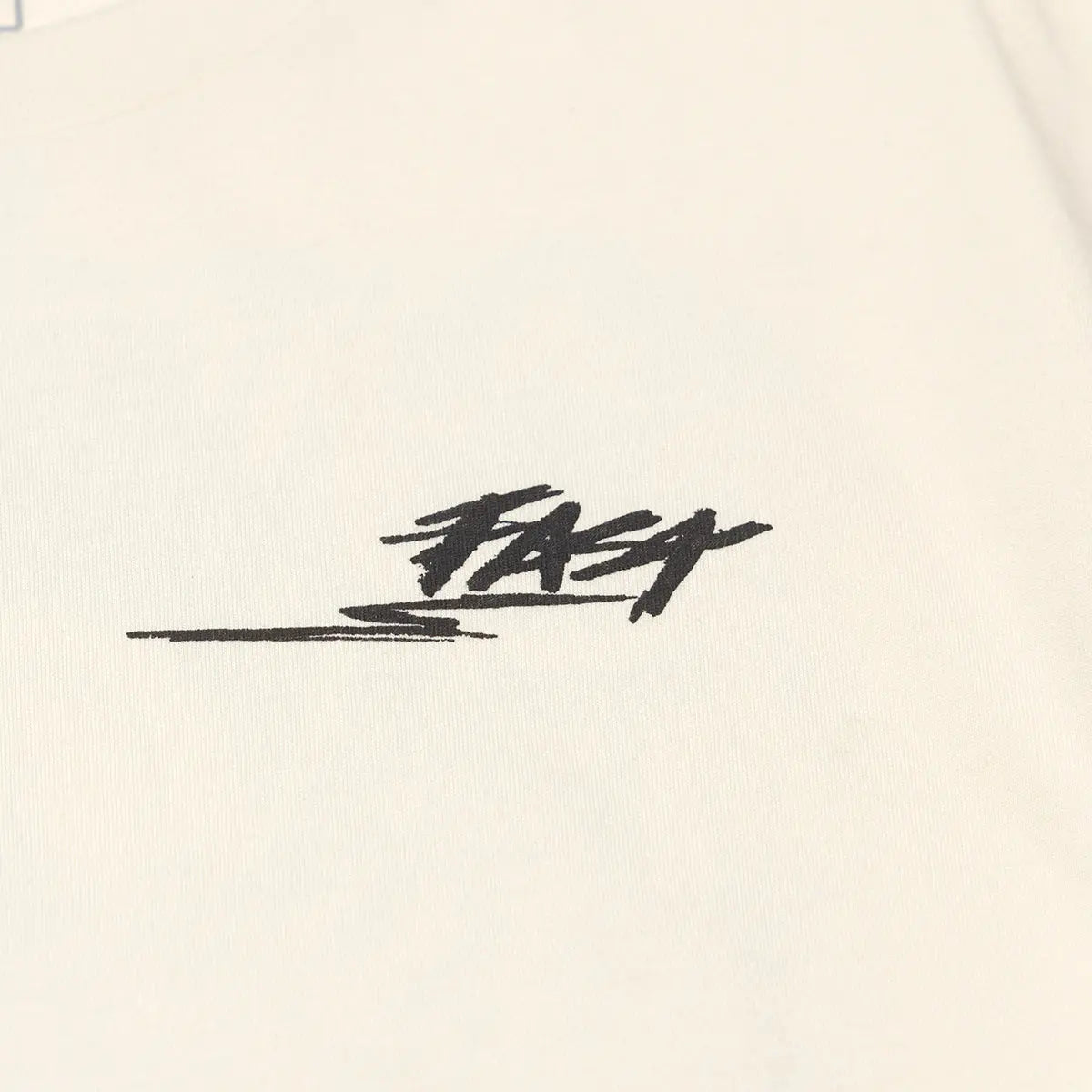 Close-up of Tomahawk Natural Tee showing Black embroidered script signature with horizontal line detail on natural cotton