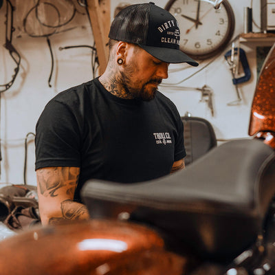 Person wearing DHCM Classic Trucker White/coyote Brown Hat, Man wearing black trucker hat in cluttered garage workshop with