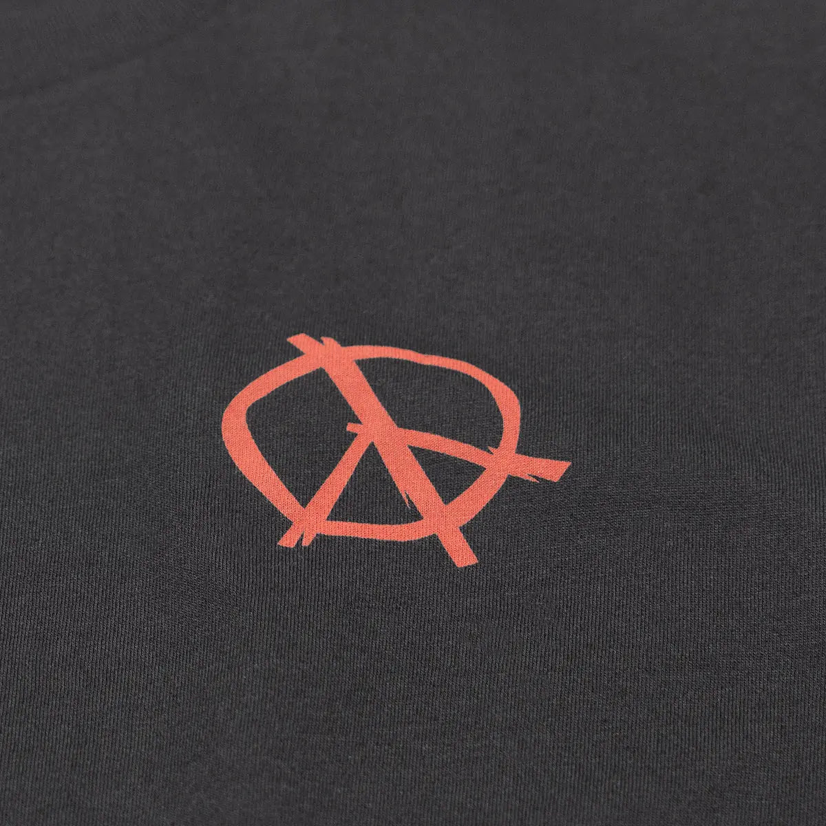 Close-up of Utopia Black Tee showing Coral anarchy symbol embroidered on charcoal fabric with visible stitch texture -