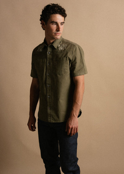 Person wearing Westy Shirt S/S Woven Light Khaki S/S Woven, Neutral studio setting with warm beige backdrop - Slowride Supply