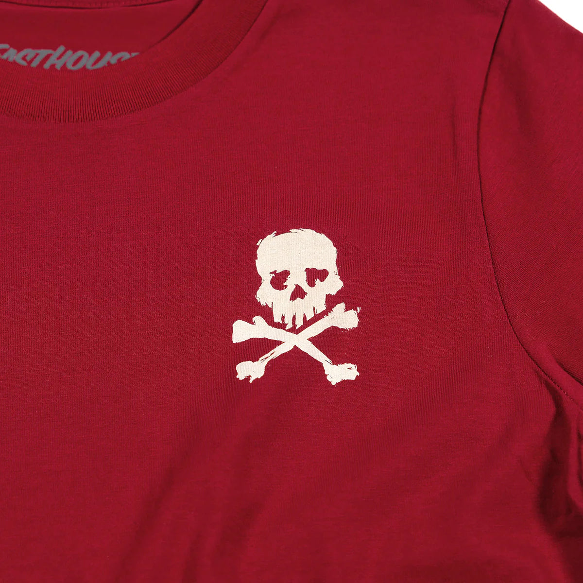 Close-up of Youth Alkyd Tee Cardinal Kids Kids Tee showing Cream skull and crossbones embroidery on cardinal red cotton