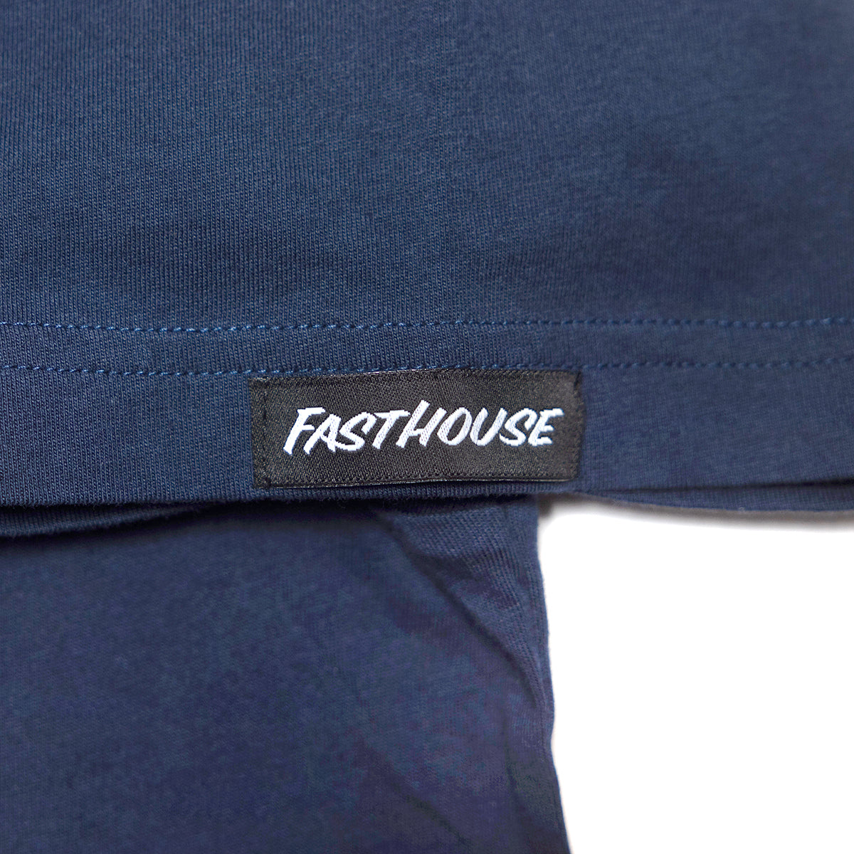 Close-up of Youth Demolition Tee Kids Navy Kids Tee showing Black woven label with white italic text on navy seamed hem -